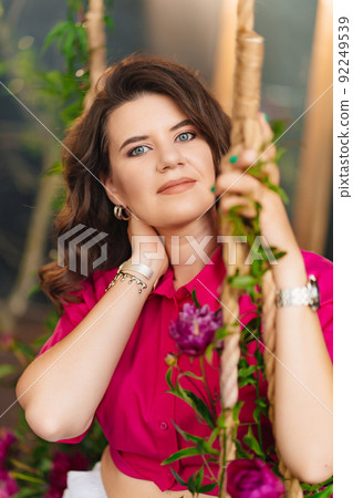 an attractive woman in a pink blouse with peonies on the swing. an attractive woman in a pink blouse with peonies on the swing. 92249539