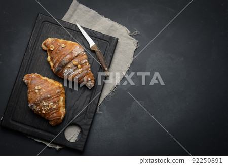 Baked croissant on a  board and sprinkled with powdered sugar, black table. Appetizing pastries for breakfast. 92250891