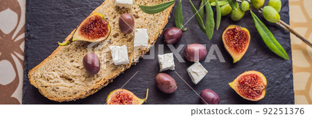 BANNER, LONG FORMAT Green and black olives with loaf of fresh bread, feta cheese and young olives branch on olive wood chopping board over dark background BANNER, LONG FORMAT Green and black olives with loaf of fresh bread, feta cheese and young olives branch on olive wood chopping board over dark background 92251376
