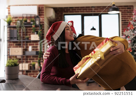 Young person receiving christmas present from coworker to celebrate xmas holiday in office with festive decorations and seasonal winter ornaments. Giving gifts to colleagues in business space. 92251551