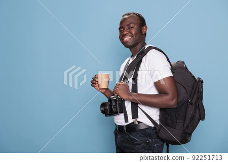 Joyful tourist having DSLR device while being excited for citybreak. Smiling heartily photography enthusiast wearing travel backpack and professional camera ready for holiday trip. 92251713