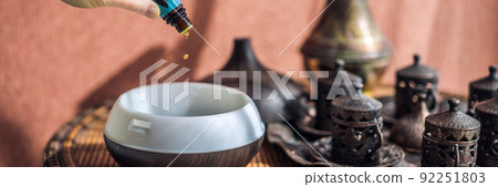 Woman adding essential oil to aroma diffuser on table BANNER, LONG FORMAT Woman adding essential oil to aroma diffuser on table BANNER, LONG FORMAT 92251803