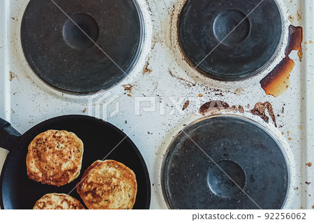 kitchen stove dirty with burnt food and cooking oil, frying pan with pancakes on top kitchen stove dirty with burnt food and cooking oil, frying pan with pancakes on top 92256062