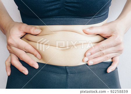 Close-up of Woman touching her fat belly, woman's hand holding excessive belly fat. Being overweight is one of the leading causes of major diseases such as heart disease, stroke, high blood pressure. Close-up of Woman touching her fat belly, woman's hand holding excessive belly fat. Being overweight is one of the leading causes of major diseases such as heart disease, stroke, high blood pressure. 92258839