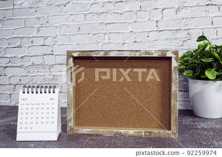 May 2022 white calendar with wooden frame and potted plant on wooden desk. May 2022 white calendar with wooden frame and potted plant on wooden desk. 92259974