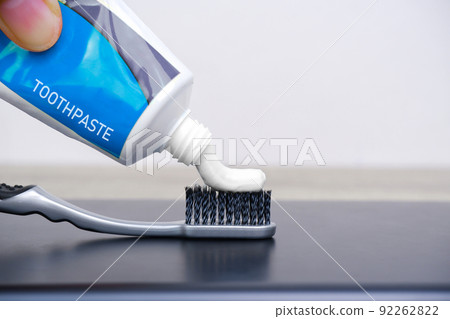 Hand squeezed white toothpaste onto a gray toothbrush 92262822