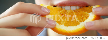 Woman hold in hand slice of chopped orange eats for breakfast with mouth in kitchen 92271032