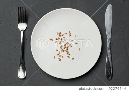 Concept of a global food crisis caused by hunger due to lack of grain. Plate with small amount of grain on plate on black background 92274344