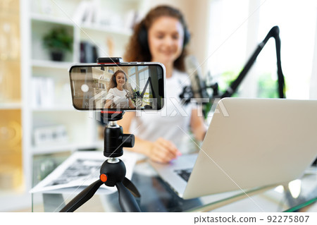 Young curly female blogger recording video at table at home 92275807