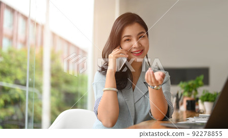 Young working woman having phone conversation with her business partner while sitting in bright modern office 92278855