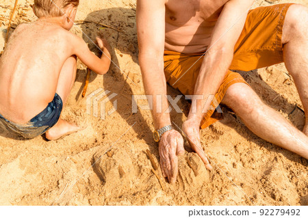 a father with vitiligo and his son play with sand on the beach on a hot summer day. Building castles. Without faces. The concept of a beach holiday. 92279492
