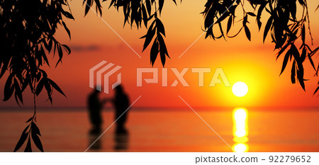 Blurred silhouette of young couple in love, standing in the sea at sunset Blurred silhouette of young couple in love, standing in the sea at sunset 92279652