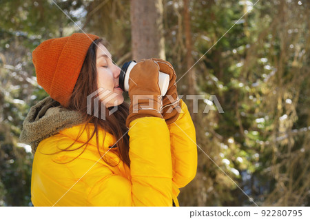 Girl in casual clothes with a glass of hot drink in her hands. Young woman in winter forest or park. Fairy forest 92280795