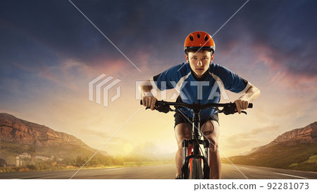 Portrait of young boy in helmet and uniform riding road on bike. Mountain landscape 92281073