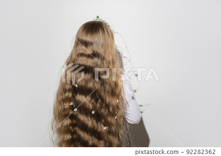 Back view of child girl with long blond wavy flowing hair and crown with a garland of snowflakes on her head. Child celebrates Christmas and Happy Birthday. Copy space for text. Soft selective focus Back view of child girl with long blond wavy flowing hair and crown with a garland of snowflakes on her head. Child celebrates Christmas and Happy Birthday. Copy space for text. Soft selective focus 92282362