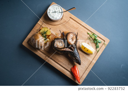 top view of roasted mackerel fish with lemon, potato and sauce on wooden board 92283732