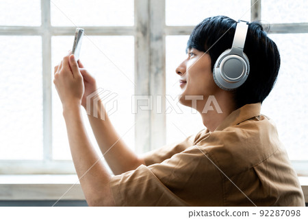 一個年輕人戴著耳機在智能手機上聽音樂 92287098