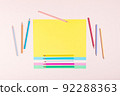 Pencils in pastel colors creatively arranged in a pattern on multicolored papers and a pink background. 92288363