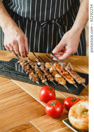 Shish kebab or kebab - pieces of beef, pork or chicken on skewers, cooked on the grill in the hands of the chef. Traditional dish of Caucasian and Asian cuisine Shish kebab or kebab - pieces of beef, pork or chicken on skewers, cooked on the grill in the hands of the chef. Traditional dish of Caucasian and Asian cuisine 92292254