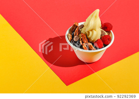 Frozen yogurt with raspberries, blueberries, chocolate drops and pecans. Hard light, deep shadow 92292369