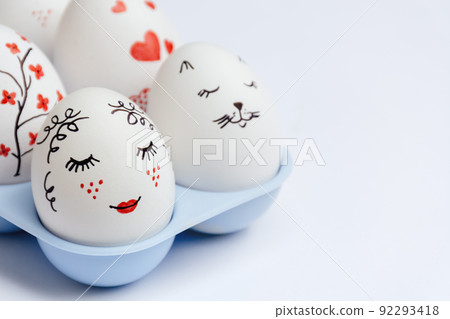Close up of beautifully painted Easter eggs - gentle beauty with red lips, cat's face, hearts and flowers in blue stand on white background. Handmade master class. Soft Selective focus. Copy Space 92293418