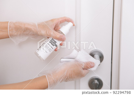 Cleaning door handles with wet wipe and white gloves. Woman hand using towel for cleaning home room door link. Sanitize surfaces prevention in hospital and public spaces against corona virus. 92294798