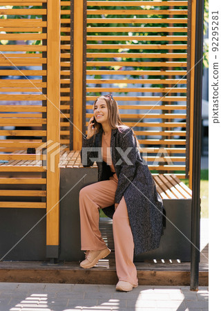 A young woman is talking on the phone, sitting on a city bench A young woman is talking on the phone, sitting on a city bench 92295281