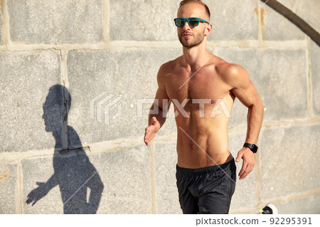 Urban sports. Sporty man shirtless jogging for fitness in the city park on a beautiful summer day 92295391