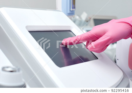 Doctor cosmetologist adjusts the device for photorejuvenation using the touchscreen 92295416