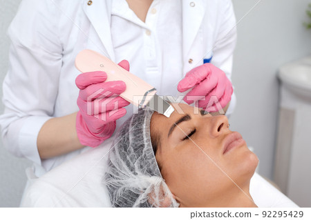Beautiful woman receiving ultrasound cavitation facial peeling. Cosmetology and facial skin care Beautiful woman receiving ultrasound cavitation facial peeling. Cosmetology and facial skin care 92295429
