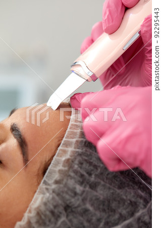 Cosmetologist, beautician in pink gloves making facial treatment with ultrasonic spatula to woman, face skin scrubber treatment with ultrasonic spatula, facial cleansing procedure in beauty salon Cosmetologist, beautician in pink gloves making facial treatment with ultrasonic spatula to woman, face skin scrubber treatment with ultrasonic spatula, facial cleansing procedure in beauty salon 92295443