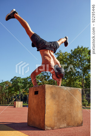 Sporty physically fit man doing step-up exercise on wooden box while doing gym training in sports club. Sporty physically fit man doing step-up exercise on wooden box while doing gym training in sports club. 92295446