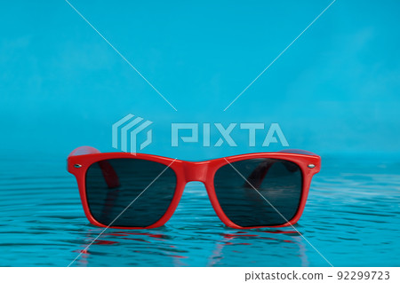 Red sunglasses in blue water, the concept of relaxing on the beach. Copy space. Red sunglasses in blue water, the concept of relaxing on the beach. Copy space. 92299723