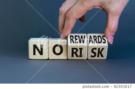 No risk or rewards symbol. Businessman turns wooden cubes and changes words 'no risk' to 'no rewards'. Beautiful grey background. No risk or rewards and business concept. Copy space. 92301617