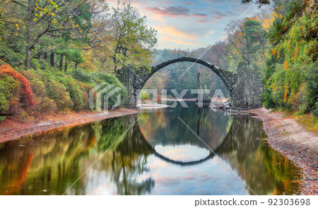 Fabulous autumn landscape in Azalea and Rhododendron Park Kromlau. Rakotz Bridge (Rakotzbrucke, Devil's Bridge) 92303698