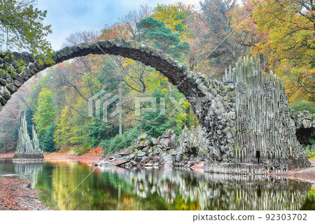 Fabulous autumn landscape in Azalea and Rhododendron Park Kromlau. Rakotz Bridge (Rakotzbrucke, Devil's Bridge) 92303702