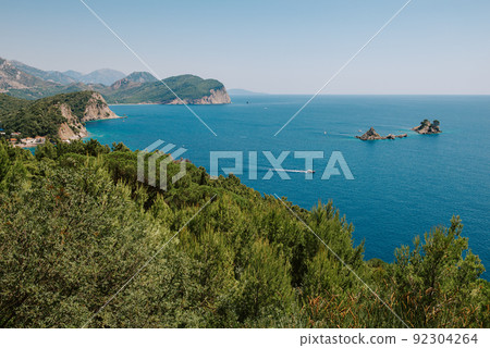 Picturesque view on rocks on a sunny day from the sea. Budva riviera, Montenegro. Aerial view of Sveti Nikola, Budva island, Montenegro. Hawaii beach, umbrellas and bathers and crystal clear waters 92304264