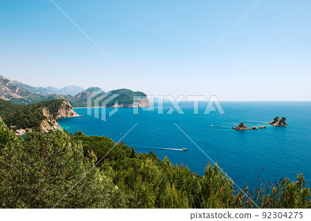 Picturesque view on rocks on a sunny day from the sea. Budva riviera, Montenegro. Aerial view of Sveti Nikola, Budva island, Montenegro. Hawaii beach, umbrellas and bathers and crystal clear waters 92304275