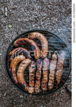 Summer grilling food, sausage, vegetables and kebab meat on barbecue grill over smoke and hot charcoal 92306884