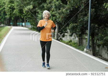 Athletic asian senior woman running outdoor jogging in park. 92312751