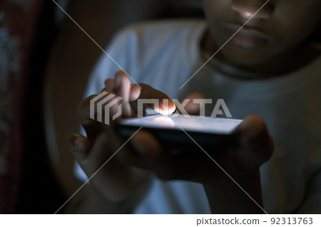teenage boy sitting on sofa using smart phone at night teenage boy sitting on sofa using smart phone at night 92313763