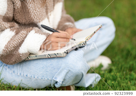 Girl writing notes with pen while sitting in the street. Girl writing notes with pen while sitting in the street. 92323999
