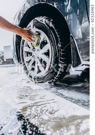 A man washes his car with foam at a self-service car wash, wheels and tires close-up. 92328463