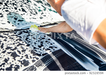 A man washes his car with foam at a self-service car wash, close-up. A man washes his car with foam at a self-service car wash, close-up. 92328594