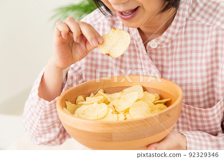 Middle woman eating potato chips in the bedroom 92329346