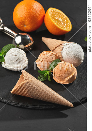 Close-up shot of a creamy and orange ice cream served on a dark slate, black background. 92332964