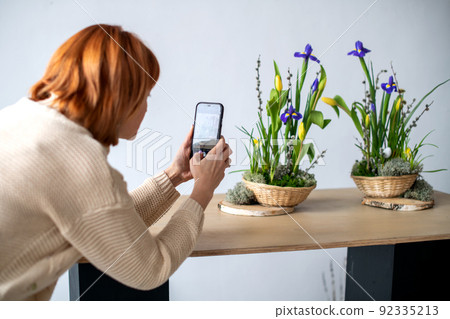 An unrecognizable woman takes pictures on her mobile phone of elegant spring, Easter flower arrangements made of daffodils, located on a table in daylight at home An unrecognizable woman takes pictures on her mobile phone of elegant spring, Easter flower arrangements made of daffodils, located on a table in daylight at home 92335213