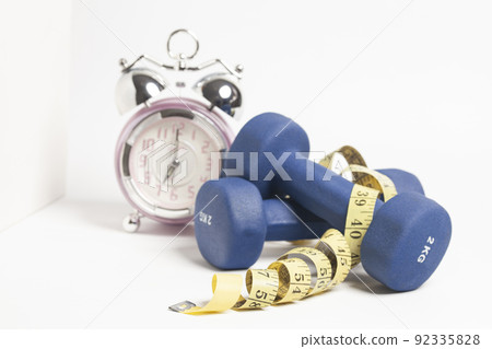 Time for exercising alarm clock,yellow measuring tape and dumbbell isolated on a white background Time for exercising alarm clock,yellow measuring tape and dumbbell isolated on a white background 92335828