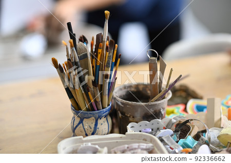 Ceramics making equipment with paint brushes, pottery shaping tools on wooden table in creative studio Ceramics making equipment with paint brushes, pottery shaping tools on wooden table in creative studio 92336662