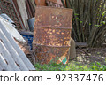 Metal barrel covered with corrosion close-up. An old rusty barrel stands next to a metal scrap. 92337476